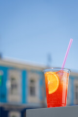 refreshing summer cocktail. A cold orange drink in a takeaway glass against the background of the street. Sale of summer drinks lifestyle