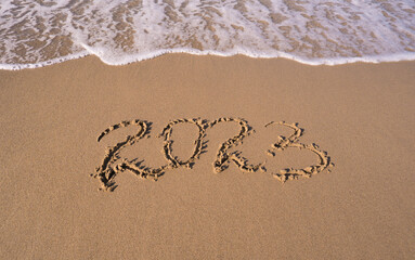 Hand-drawn numbers 2023 of new year on wet yellow sand on beach, copy space.