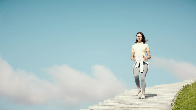 Fitness young adult woman running on stairs. Female workout on sky background. Amazing view stairs to haven. Active sports person jogging and reaching the aim.