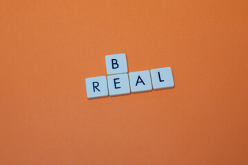 Be real text with plastic letters on orange paper sheet. Popular and trendy mobile app called Be Real is spreading around the globe. Be realistic yourself is a good way of living your life.