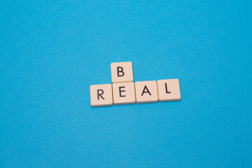 Be real text with plastic letters on blue paper sheet. Popular and trendy mobile app called Be Real is spreading around the globe. Be realistic yourself is a good way of living your life.