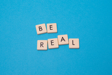 Be real text with plastic letters on blue paper sheet. Popular and trendy mobile app called Be Real is spreading around the globe. Be realistic yourself is a good way of living your life.