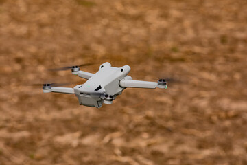 Modern drone with rotating rotors and camera cut out hovering over a field
