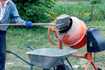 A worker shovels sand into a concrete mixer, preparing cement mortar