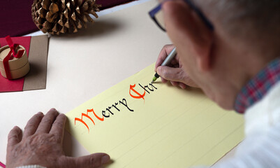An elderly man writes with pen and ink and gothic style a Christmas card. Hand calligraphy 