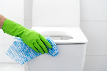 person in gloves cleaning toilet with cloth rag in bathroom, closeup