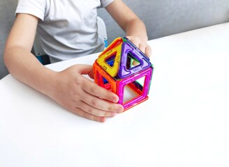  a child plays with a magnetic constructor on a white table. Game with a magnetic constructor for development. child playing with toy blocks