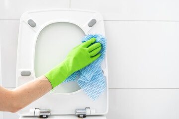 person in gloves cleaning toilet lid with cloth rag in bathroom