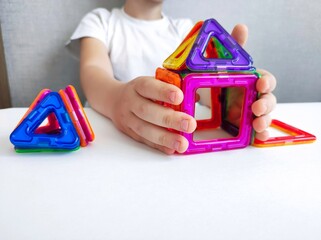 a child plays with a magnetic constructor on a white table. Game with a magnetic constructor for...