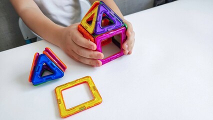 a child plays with a magnetic constructor on a white table. Game with a magnetic constructor for...