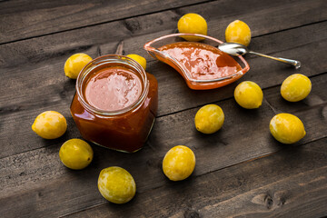 yellow plums on a wooden table and a jar of plum jam