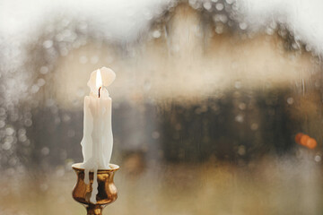 Cozy autumn rainy day. Stylish burning candle against window with rain drops. Autumn banner.  Moody...