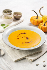 One deep grey soup bowl with an orange pumpkin cream soup with pumpkin seed oil, on a gray concrete background