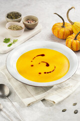 One deep grey soup bowl with an orange pumpkin cream soup with pumpkin seed oil, on a gray concrete background