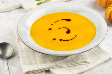 One deep grey soup bowl with an orange pumpkin cream soup with pumpkin seed oil, on a gray concrete background