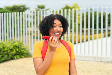 Fototapeta premium Smiling woman sending a voice message via cell phone in the park.