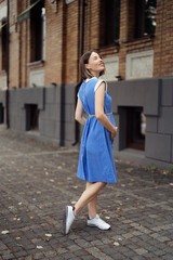Fototapeta premium Happy pregnant woman chilling and having fun while walking in the city in a midi blue vintage dress. Happiness all around