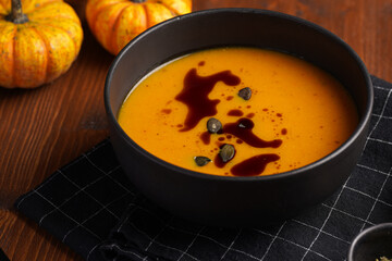 One deep black bowl with an orange pumpkin cream soup with pumpkin seed oil, two black spoons on a wooden surface