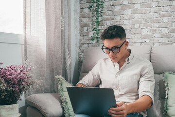 One young happy man surfing the net using his laptop at home sitting on the sofa enjoying free time and relaxing alone. Entrepreneur boy working and building his future..