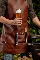 man who is going to make a barbecue with apron holding a glass of beer in his hand