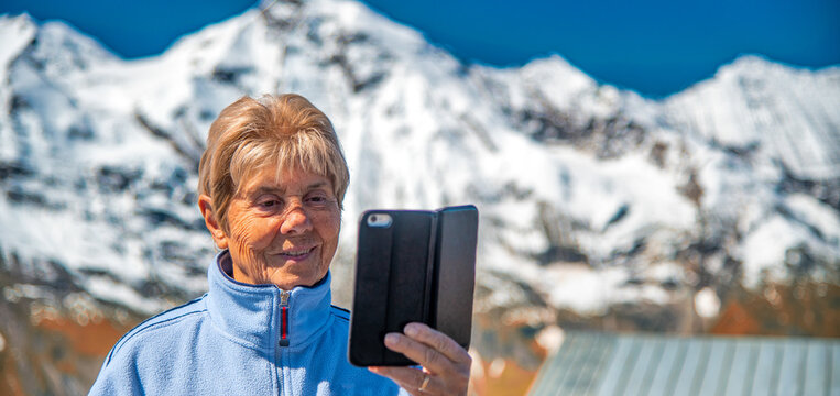 Happy retired elderly woman taking pictures of a beautiful summer mountain landscape.