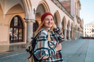 Obraz premium Rear view of 30s traveler woman carrying backpack on her shoulders visiting old city of Krakow, active lady enjoying travel and discovery. 