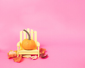 Orange pumpkin on beach chair on bright pink background with copy space. Creative autumn concept...