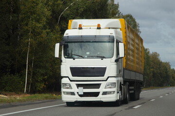 Fototapeta na wymiar White hauler truck with yellow semi trailer move on countryside highway road front view. Goods import in Europe