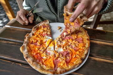 Man eating pizza from plate on wooden table in outdoor restaurant.