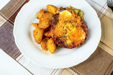 Beef burger with fried egg, baked potato and pickled cucuber on white plate.