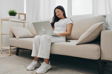 Asian woman sits with laptop and phone in home freelancer's hangout with staring at laptop screen working, lifestyle work and home