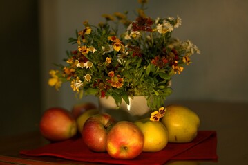 Autumn still life, bouquet of flowers on the table, in the foreground ripe apples on a red cloth