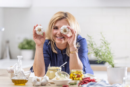 Woman uses garlic head as a telescope to look through during garlic preserving session in her kitchen
