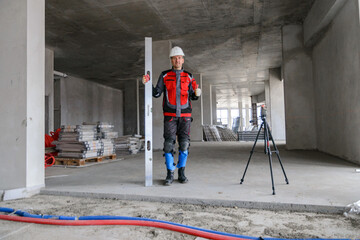 A foreman at a construction site in work clothes controls the work process, takes the necessary measurements