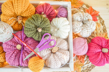 colorful woolen crochet pumpkins with woolen balls, autumn leaves and lights on a wooden tray