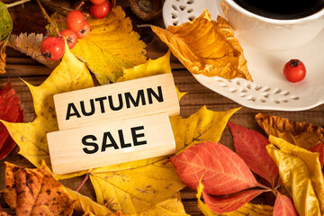 Autumn sale concept wooden block with the inscription, Colorful leaves, cup with hot coffee, viburnum fruits, Background from old boards