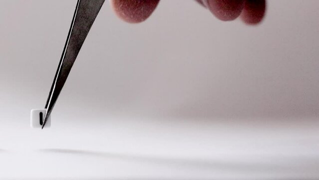 Announcement It Is A Girl assembled of letters made out of tiny white plastic cubes by a hand with tweezers on flat background. Newborn baby girl celebration.