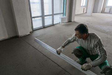 A builder in work clothes does his job, levels the floor and pours mortar