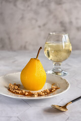 Delicious homemade autumn dessert: pears boiled in white wine. Pears in white wine with caramel and a glass of white wine on a light marble table. Light fruit dessert.