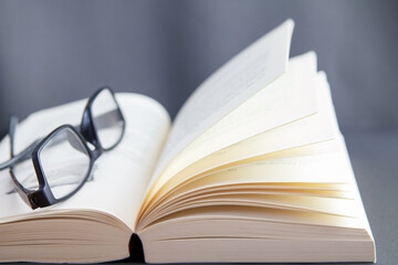 aufgeschlagenes Buch mit einzelnen Seiten aufgefächert mit Lesebrille