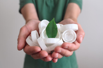 Hands holding a handful of white plastic lids and cap with green leaf. Concept of environmental pollution and eco friendly behavior. waste sorting and plastic recycling. 