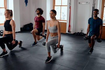 Group of multiracial young adults doing lunges with weights at the gym