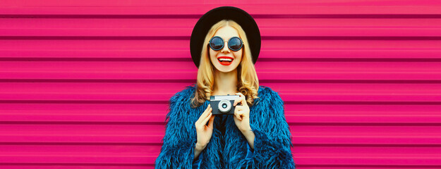 Portrait of stylish happy smiling young woman photographer with film camera taking picture wearing...
