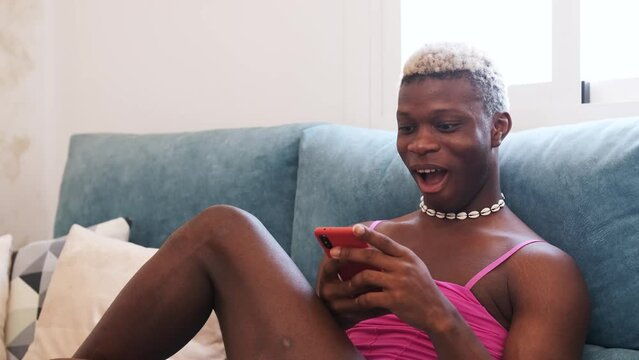 African Black transsexual man in stylish feminine clothes texting on cellphone on couch