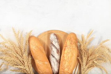 Freshly baked homemade bread, french sourdough baguette with crispy crust and ears of rye and wheat on old concrete background with space for text, modern bakery concept, healthy natural food, 