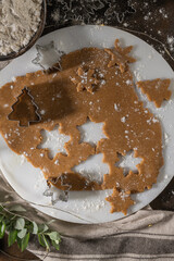 Making christmas gingerbread cookies. Raw dough in shape of gingerbread man, christmas tree, star, snowflakes on paper on tray on rustic table with rolling pin. Preparing for baking