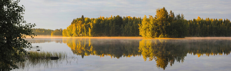 Panorama of golden fall colors reflecting on a still lake