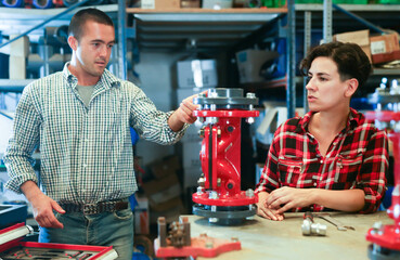 Woman fixing and assembling plumbing fixture in workshop. Her mentor talking to her, giving advices.