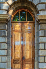 Fototapeta na wymiar French Style Hardwood Doors with a Arched Window on a Gray Building.