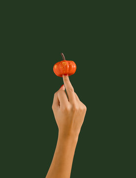 Woman's hand shows aggresive gesture with the middle finger and pumpkin on dark green background. Autumn colors. Seasonal background.